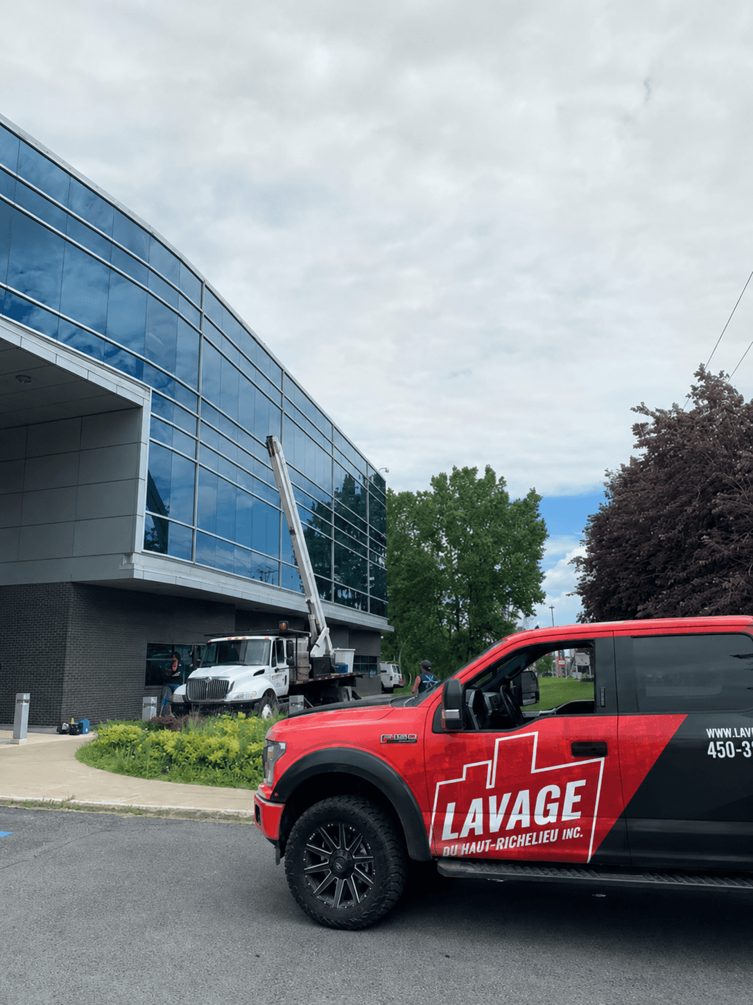 Camion lettré Lavage du Haut-Richelieu devant un immeuble institutionnel, nacelle en action